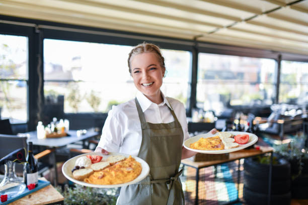 Smiling young waitress serving guests their dinner at nice restaurant. 