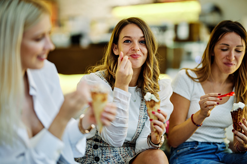 Three girls sitting in cafe and eating ice cream.