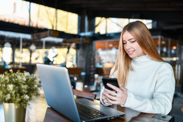 istock Cute Female Freelancer Contacting Customers Via Smartphone While Working On Laptop In Coffee Bar 1360391556