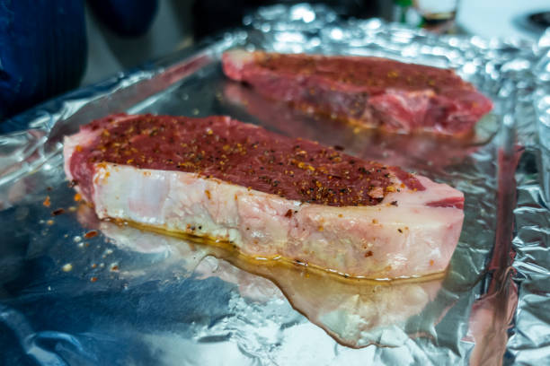 vista angolata di due grandi bistecche crude, appena condite su una teglia ricoperta di carta stagnola - strip steak aluminum foil steak foto e immagini stock