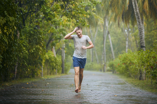 Drenched young man runing on road in heavy rain.