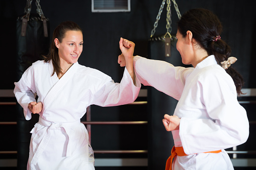 Two women in kimono and belt fighting with opponent during group karate training.
