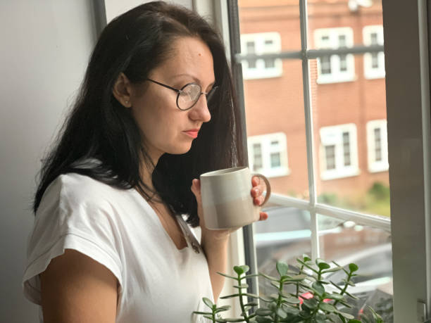 istock Young woman is drinking coffee by the window. Deep in thoughts 1360403299