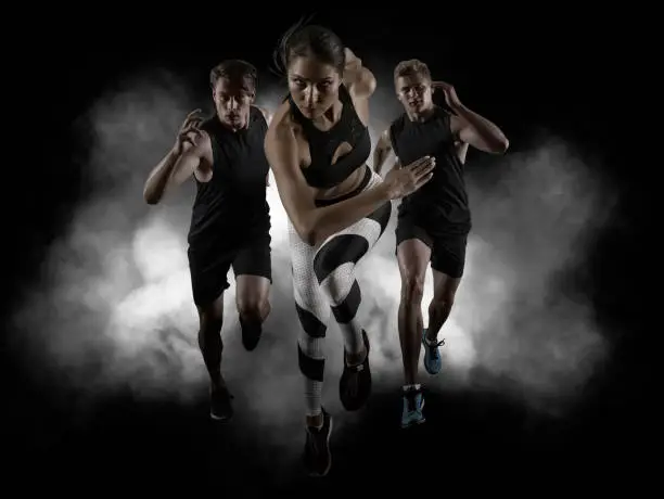 Sporty young woman and men running on black background