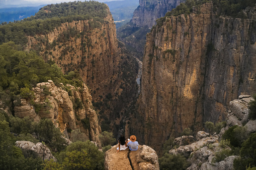 Tourist stylish couple sitting on the edge of a cliff against the backdrop of a gorge. Amazing Tazi Canyon ,Bilgelik Vadisi in Manavgat, Antalya, Turkey. Greyhound Canyon, Wisdom Valley.