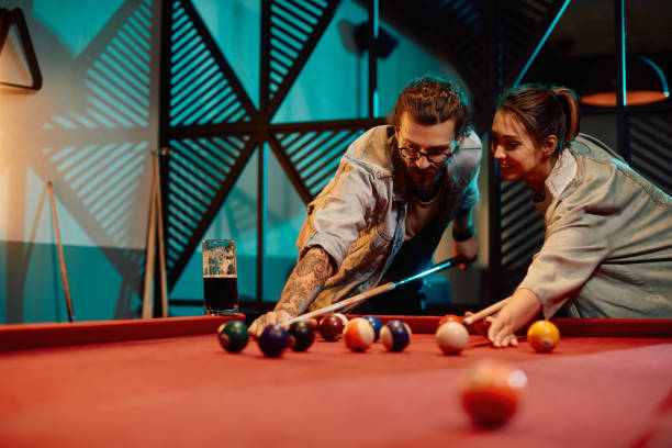 Young man teaching his girlfriend to play snooker in a pool hall.