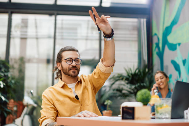 istock Young man with hand raised calling the waiter in a cafe. 1360408331