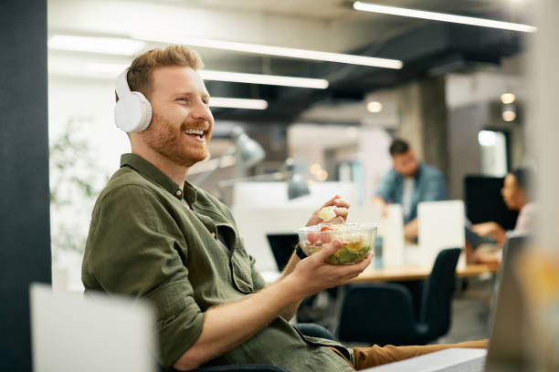 happy freelance worker listening music while having lunch break at corporate office. - health profession imagens e fotografias de stock