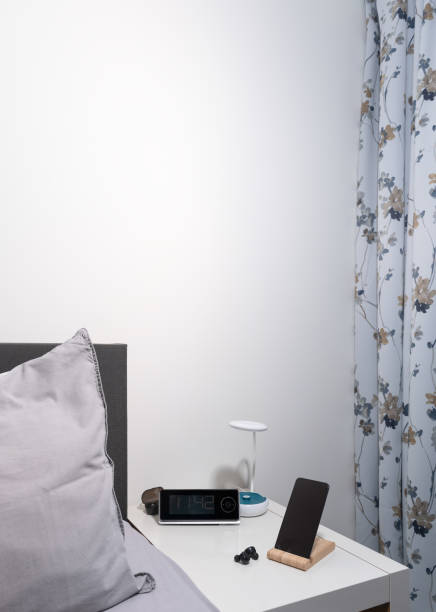 istock smartphone on the bedside table with lamp, headset, clock and bed as background. vertical 1360410395