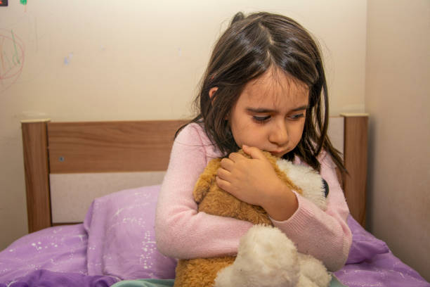 Scared little girl sitting on bed hugging her teddy bear, anxiety disorder Scared little girl sitting on bed hugging her teddy bear, anxiety disorder Phobia stock pictures, royalty-free photos & images