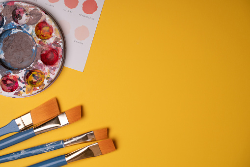 Artist workspace. Paintbrushes, color palette and watercolors against a bright yellow background