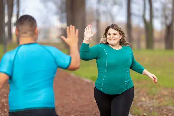 Plus size couple training and running outdoors. They are doing some cardio exercises for weight loss after quarantine period. While jogging they passing by each other