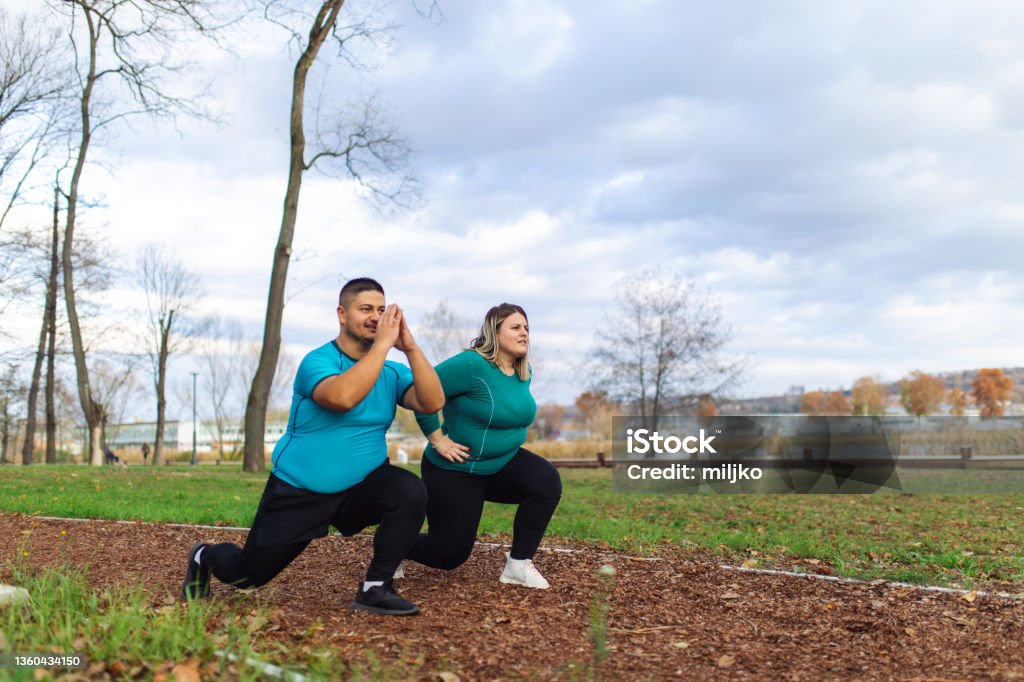 People with overweight problem exercising in city park Plus size couple training and running outdoors. They are doing some cardio exercises for weight loss after quarantine period Obesity Stock Photo