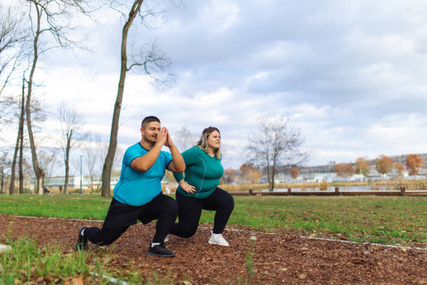 Pessoas com problemas de sobrepeso se exercitando em parque da cidade. Casal plus size treinando e correndo ao ar livre. Eles estão fazendo exercícios cardiovasculares para perder peso após o período de quarentena. Fotos de pessoas obesas se exercitando, fotos e imagens livres de direitos autorais.