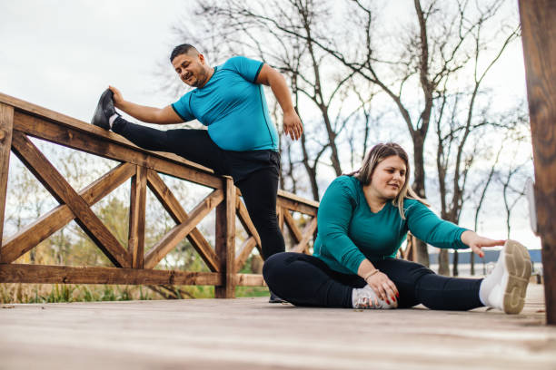 People with overweight problem exercising in city park Plus size couple training and running outdoors. They are doing some cardio exercises for weight loss after quarantine period body positive couple stock pictures, royalty-free photos & images