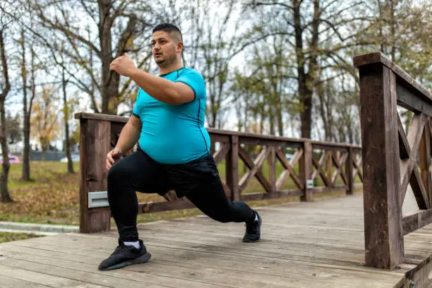 Plus size man training and running outdoors. He is doing some cardio exercises for weight loss after quarantine period