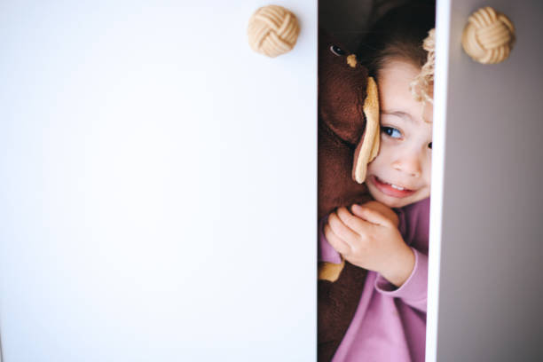 Little girl looking out of wooden open door wardrobe