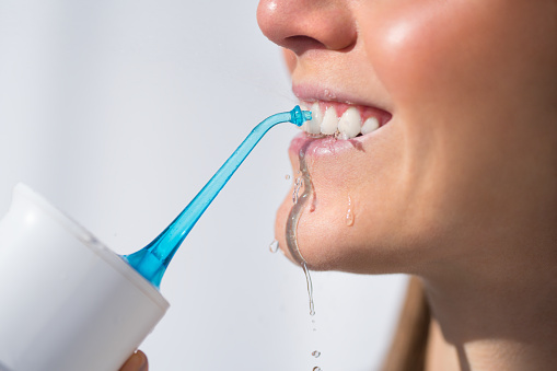 Woman with perfect white smile using portable water flosser or oral irrigator. High quality photo