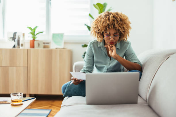 home office: una mujer afroamericana mirando una computadora portátil - trabajando en casa fotografías e imágenes de stock