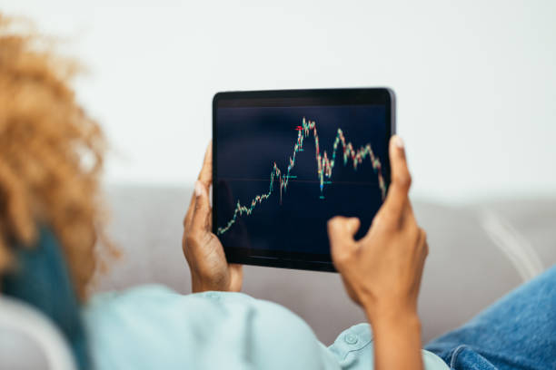 istock Home Office: An  Anonymous Afro-American Woman Using a Digital Tablet for Online Trading While Working From Home 1360438611