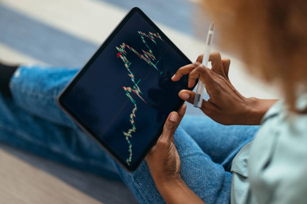 istock Home Office: An  Anonymous Afro-American Woman Using a Digital Tablet for Online Trading While Working From Home 1360439112