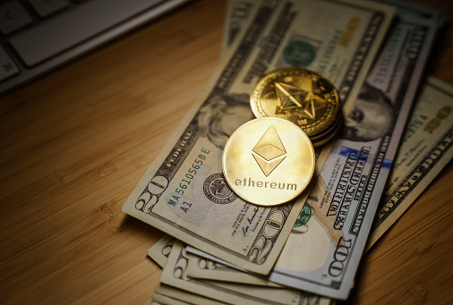 Antalya, Turkey - 23 December 2021: Close up of Ethereum golden coins on US dollar bills with spotlight on the Ethereum in the foreground.