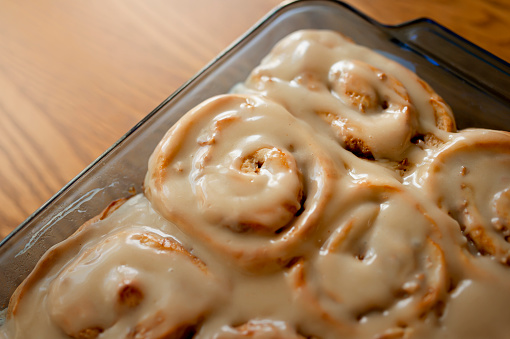 Freshly baked apple cinnamon rolls with browned butter maple icing in a glass cookware container