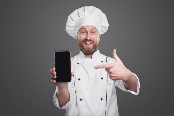istock Cheerful chef showing smartphone with black screen 1360448697