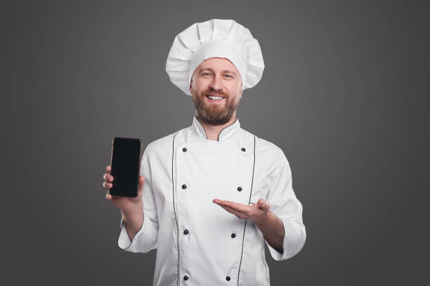 istock Cheerful chef demonstrating smartphone with blank screen 1360448702