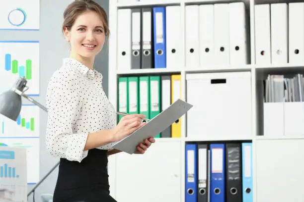 Photo of Smiling employee woman posing in conference room, making notes on paper