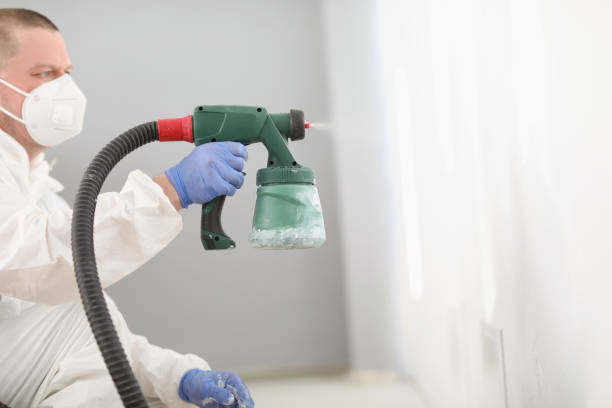 istock Worker using spray gun for coloring wall in white. Effective and fast way to paint wall 1360448816