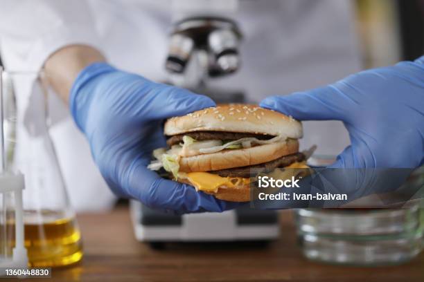 Male Chemist Holding Tasty Burger In Hand With Blue Protective Glove Stock Photo - Download Image Now