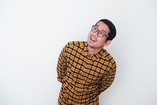 Adult Asian man wearing yellow flannel shirt looking above him with surprised expression