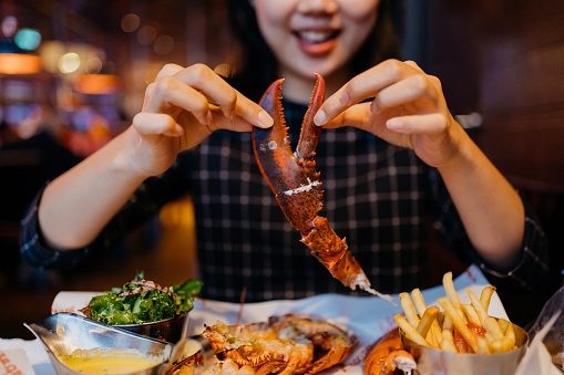 Smiling Asian woman holding a grilled lobster claw in restaurant