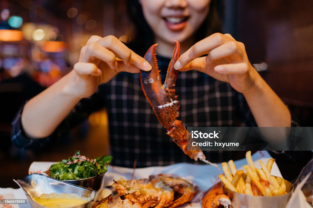 Smiling Asian woman holding a grilled lobster claw in restaurant Image of an Asian Chinese woman holding lobster claw and having a grilled lobster meal in restaurant Lobster - Seafood Stock Photo