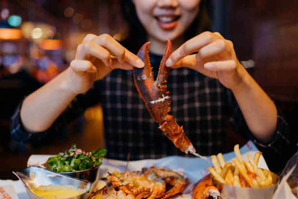 smiling asian woman holding a grilled lobster claw in restaurant - amêijoa marisco imagens e fotografias de stock