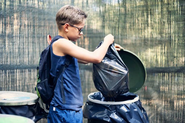 Salt Lake City, Utah, USA — September 1, 2025: A man pulls a blue recycling bin along a sidewalk bordered by grass, rocks, and a decorative metal fence.