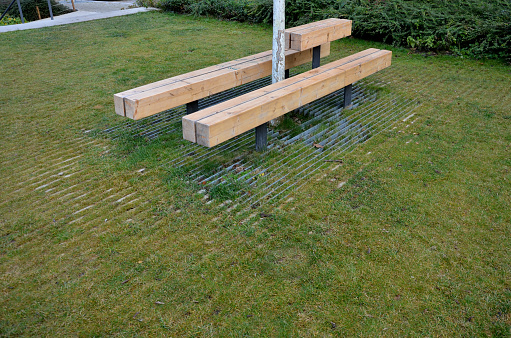 massive bench in the park under a tree in the park urban style beam shape on metal legs in the square. grass grate made of metal and concrete striped tile design with holes for soil grass turf, trunk