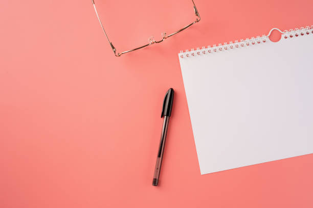 istock Top view blank calendar, glasses and pen on pink background 1360478352