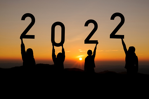 Silhouette of a group of people holding the number 2022 raised with cloud sky and sunlight in Starting to the New year concept of 2022 for new life.