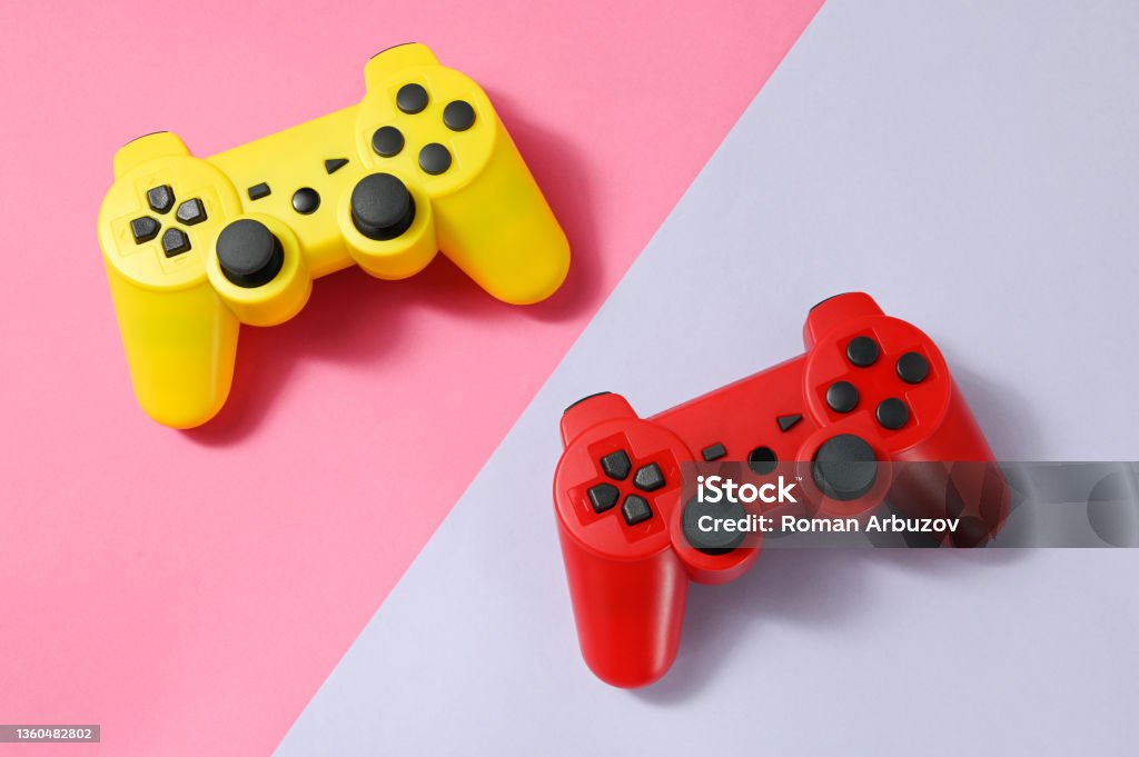Game control. Yellow and red two game control,  on pink and purple background. The concept of the competition. Game Controller Stock Photo