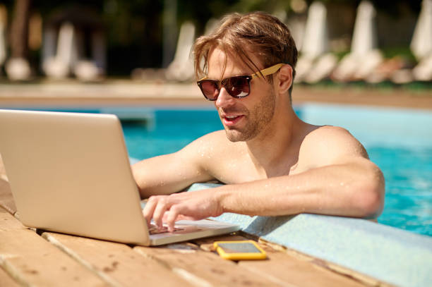 istock Young man at the swimming pool working on a laptop 1360485931