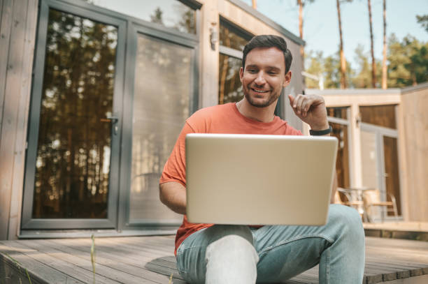 A young man with a laptop sitting outside and working online stock photo