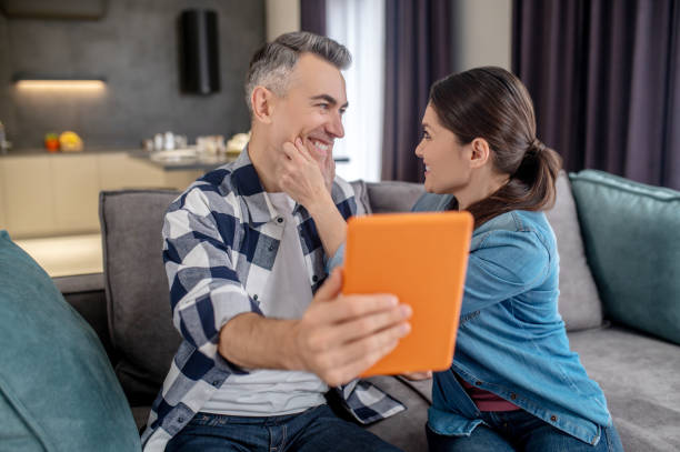istock Woman touching husband face with tablet 1360492098