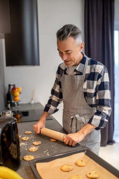 istock Man shaping cookies with rolling pin looking at table 1360492372