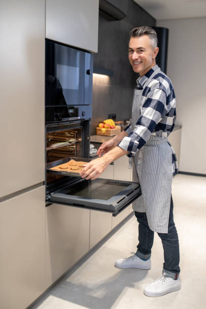 istock Man putting pan in oven looking at camera 1360492412