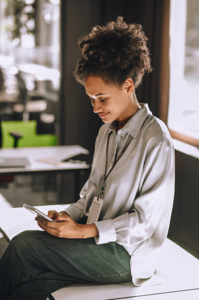 istock Curly-haired woman sitting on the table with a phone in hands 1360494626