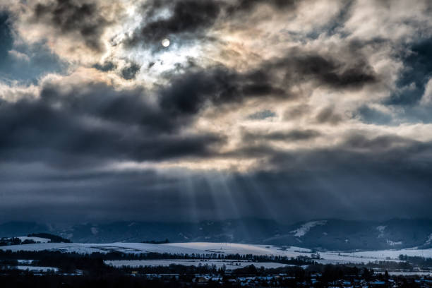 Winter snowy country and sunrays through clouds on sky.