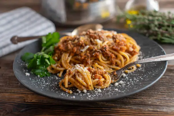 Traditional fresh cooked italian Spaghetti Bolognese with grated parmesan cheese served on a dark plate on wooden table background