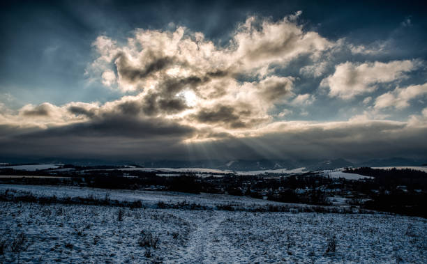 Winter snowy country and sunrays through clouds on sky.